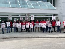 Over 20 faculty members stand in red shirts with UNAC signs in front of the UAF Butrovich Building