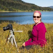 Cindy Trussell kneeling beside a camera tripod in front of a lake